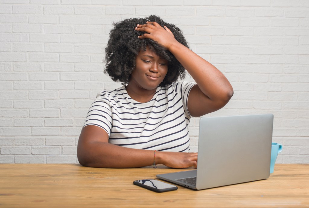 Young african american woman sitting on the table using computer laptop stressed with hand on head, shocked with shame and surprise face, angry and frustrated.
